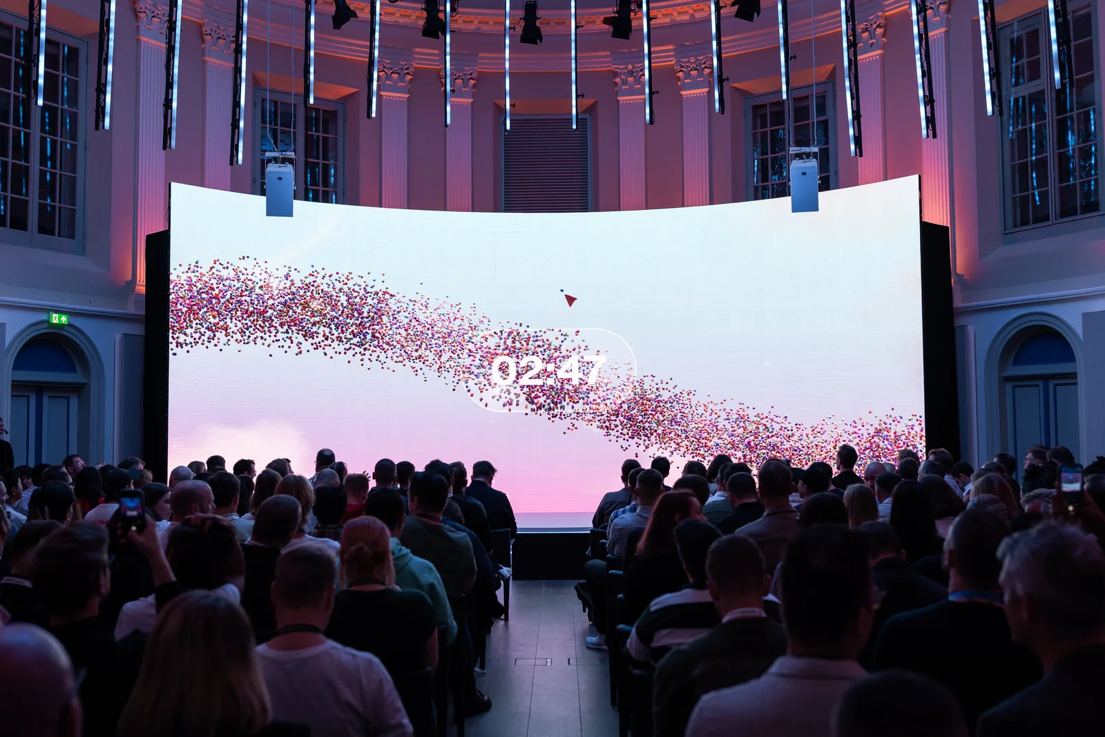 A trail of tiny coloured cubes arcs across a pink sky on the stage screen, a countdown floating over the crowd.
