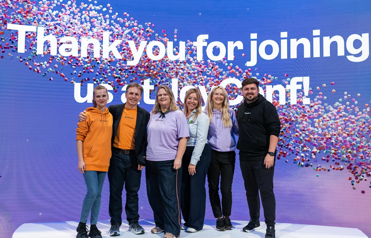Six people in Storyblok hoodies pose on stage under a screen reading "Thank you for joining us at JoyConf!"