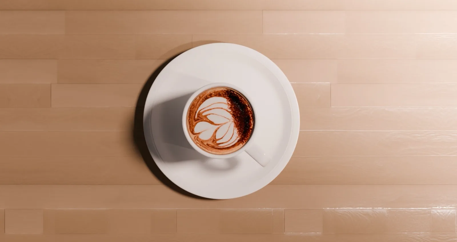 Overhead shot of a latte with leaf-pattern art dusted in cocoa, on a wooden table.